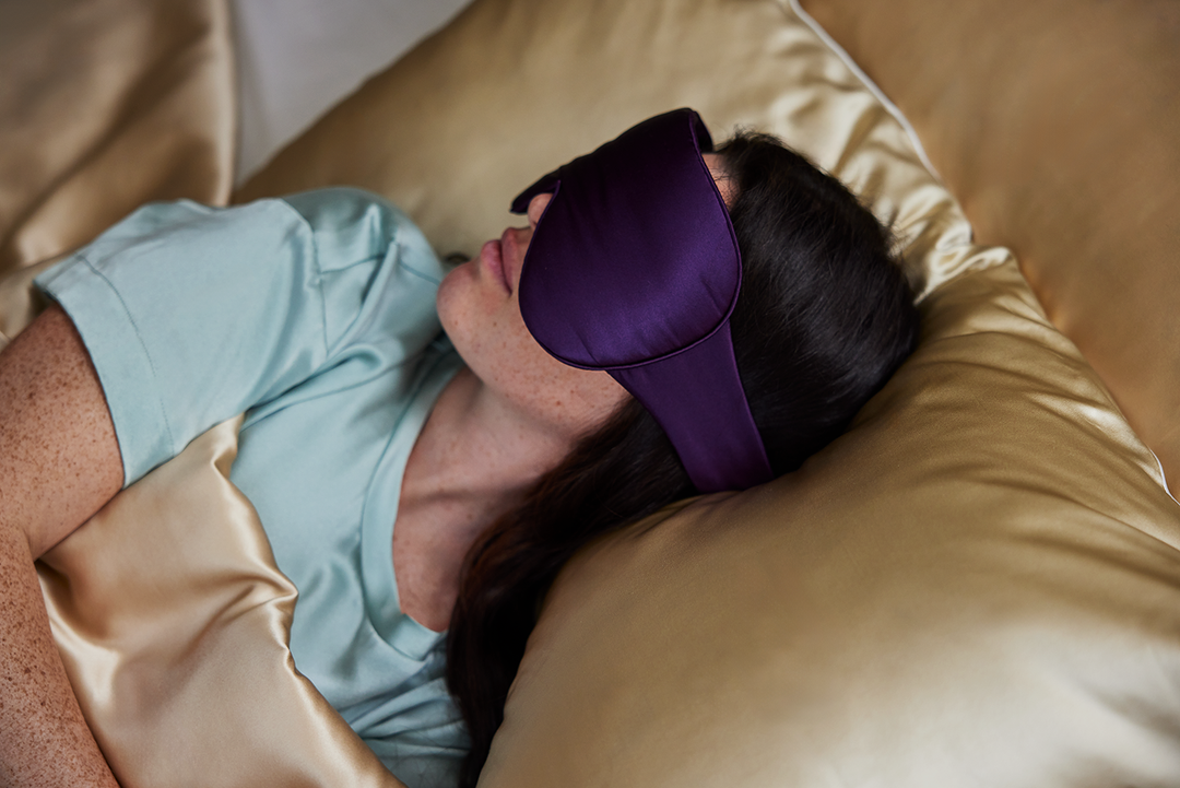 A model sleeping with the Dream Sleep Silk Eye Mask by KAILU x Dr. Andrea Matsumura in Aubergine with oversized coverage to block light and 3D optical cushion to accommodate eyelash extensions and/or gentle pressure on temples and ears