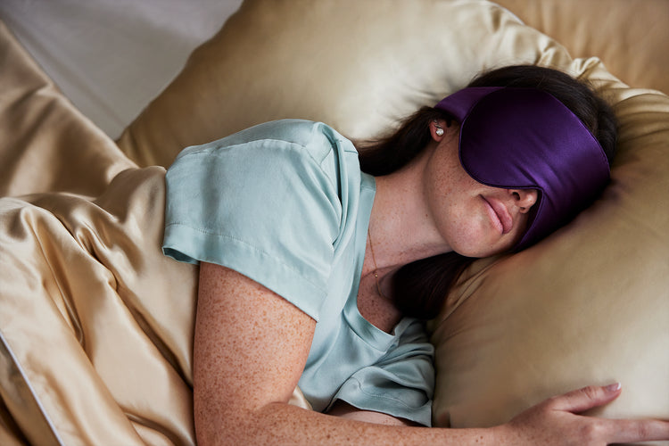 A model sleeping with the Dream Sleep Silk Eye Mask by KAILU x Dr. Andrea Matsumura in Aubergine with oversized coverage to block light and 3D optical cushion to accommodate eyelash extensions and/or gentle pressure on temples and ears