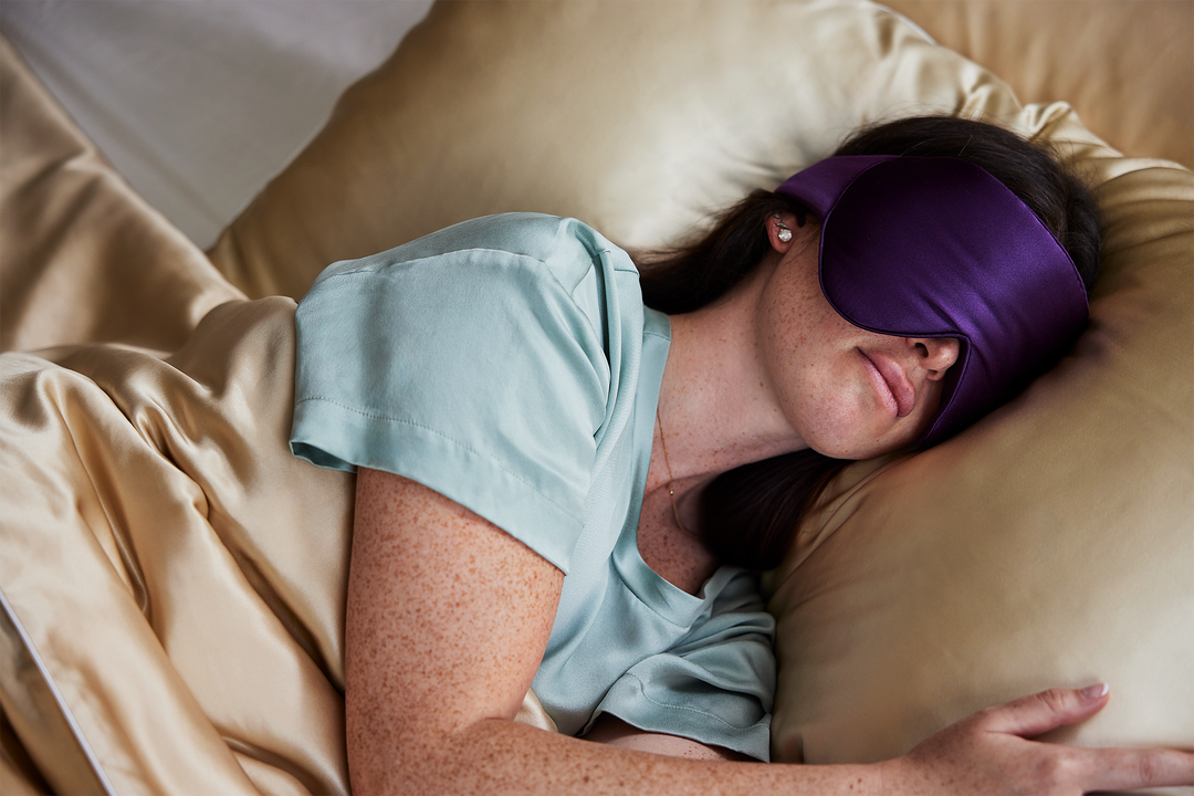 A model sleeping with the Dream Sleep Silk Eye Mask by KAILU x Dr. Andrea Matsumura in Aubergine with oversized coverage to block light and 3D optical cushion to accommodate eyelash extensions and/or gentle pressure on temples and ears